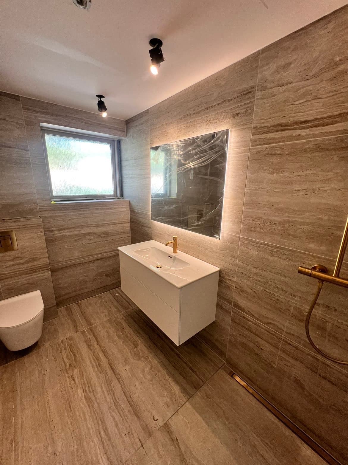 Komplet badeværelse med beige travertinfliser og guld